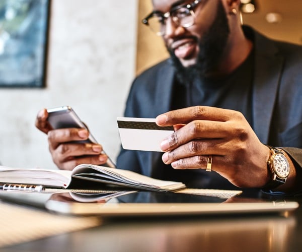 Smiling consumer holding a credit card to make an online payment using his phone